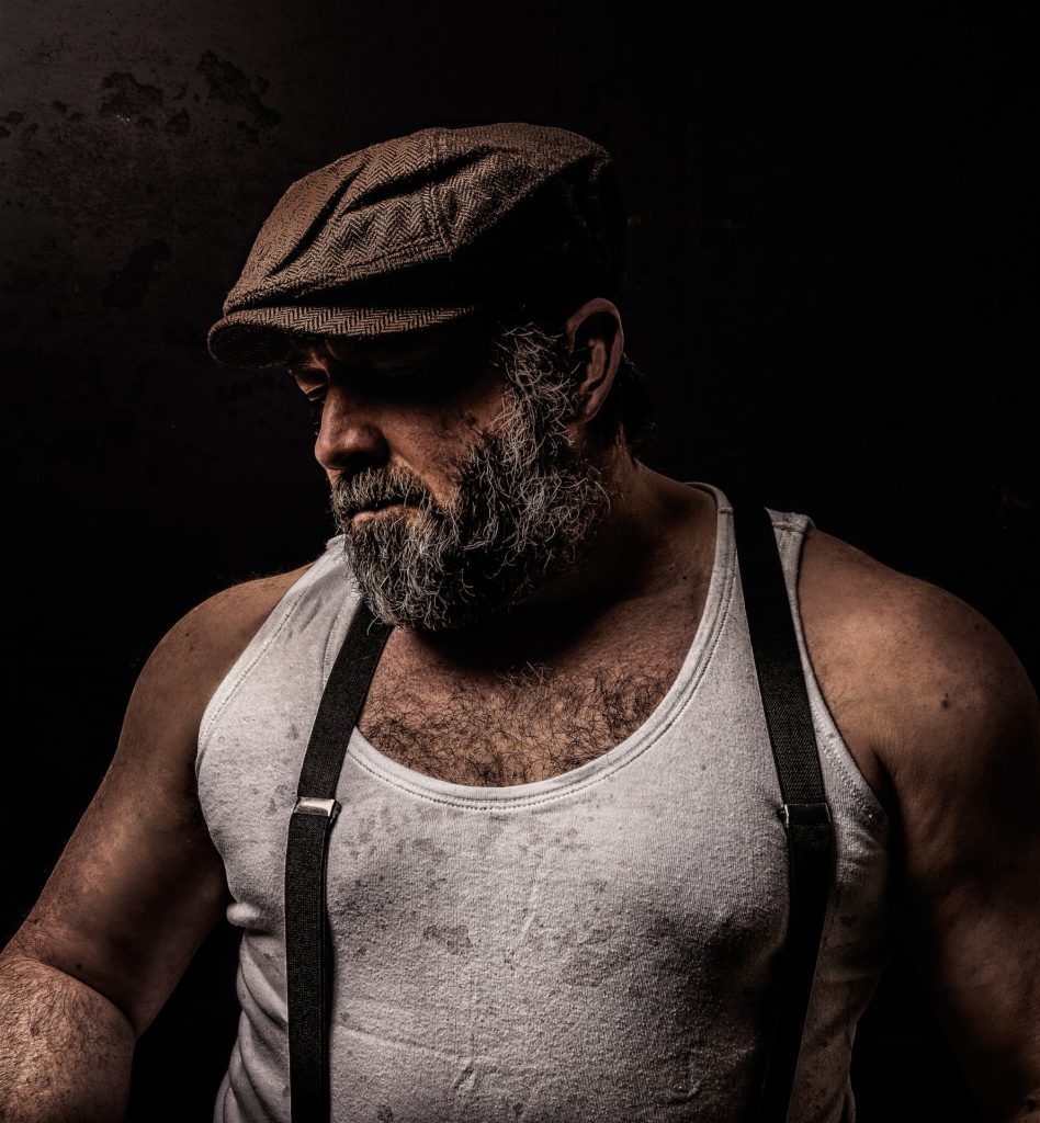 homme barbu portant casquette et bretelles, portrait de profil sur fond noir