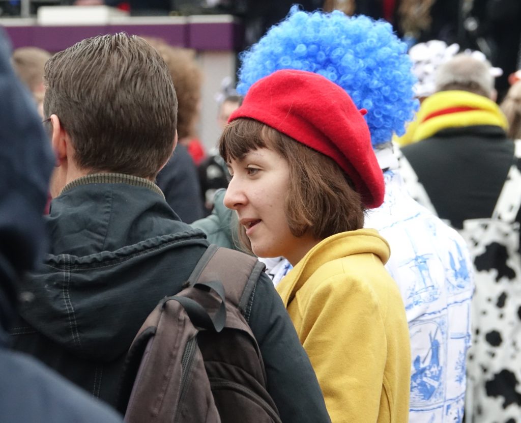 femme en beret rouge et manteau jaune dans une foule colorée