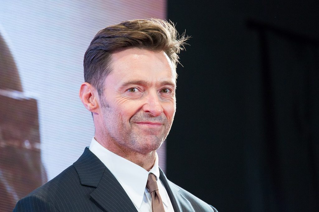 hugh jackman en costume lors d'une présentation de film, souriant légèrement vers la caméra