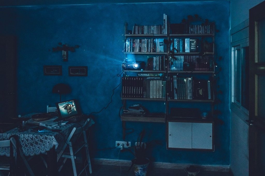 chambre baignée de lumière bleue avec étagères de dvd et ordinateur portable allumé