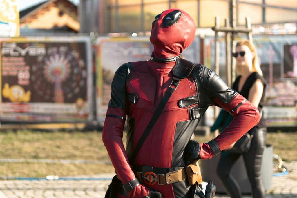 deadpool en costume rouge et noir pose devant des stands de festival