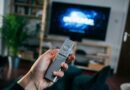 main tenant une télécommande devant un écran affichant un logo de plateforme de streaming