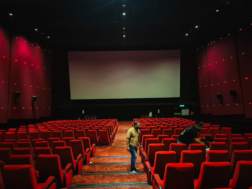 Empty cinema hall with red seats and large screen.