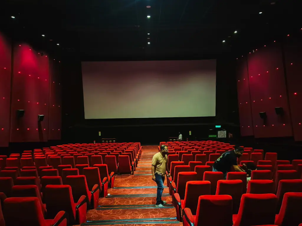 Empty cinema hall with red seats and large screen.
