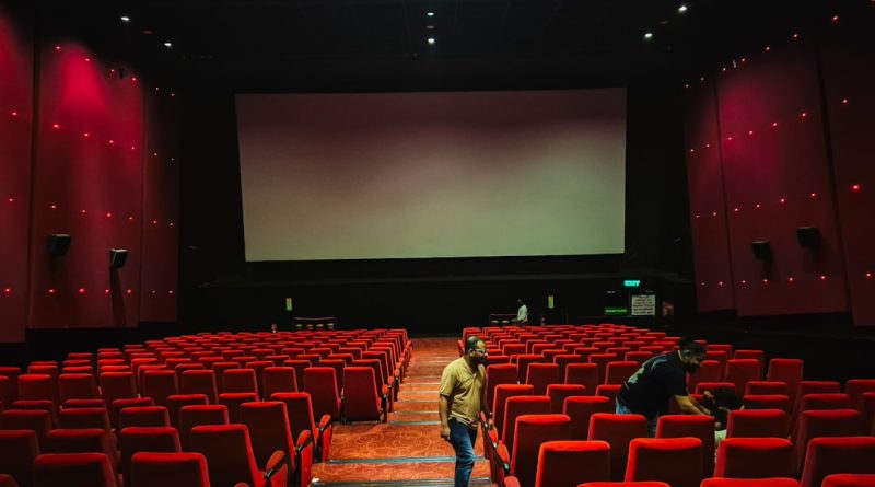 Empty cinema hall with red seats and large screen.