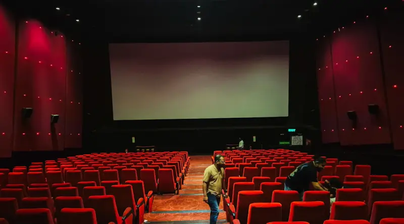 Empty cinema hall with red seats and large screen.