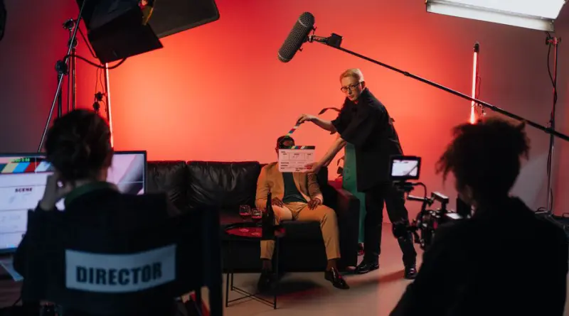 A behind-the-scenes look at a filming crew setting up a scene indoors with lighting equipment.
