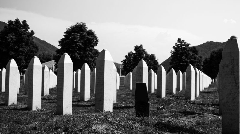 Black and white photo of the Srebrenica Genocide Memorial Cemetery in Bosnia, showcasing rows of grave markers.