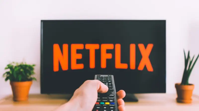 A hand holding a TV remote in front of a screen with Netflix, perfect for streaming and movie night themes.