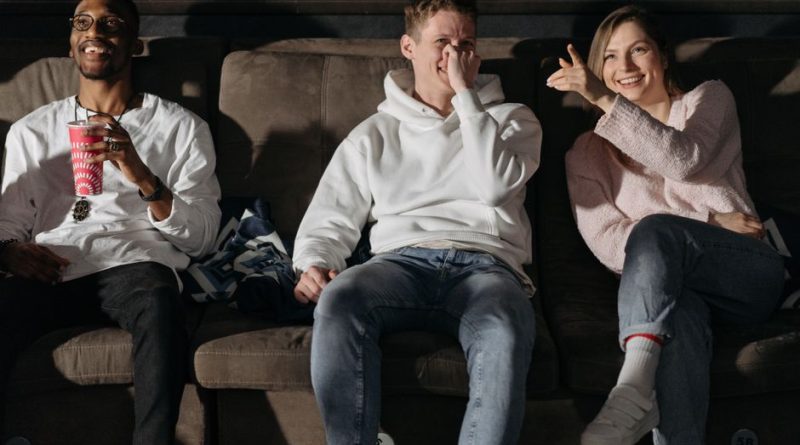 Three friends laughing and enjoying a movie in a cozy cinema setting.