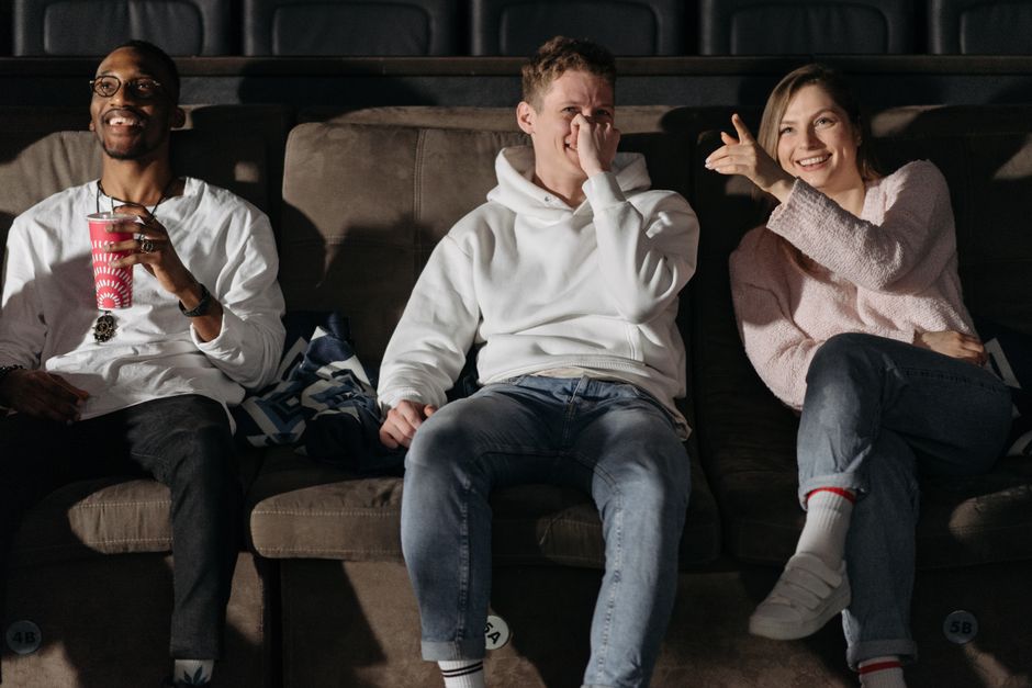 Three friends laughing and enjoying a movie in a cozy cinema setting.